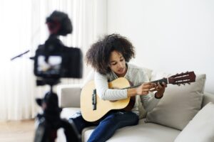 Een jongen speelt gitaar voor een camera op een statief.
